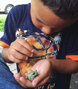 Close-up of boy holding frog while sitting outdoors