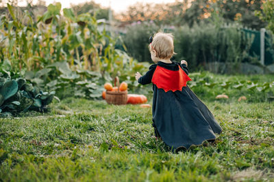 A charming kid in a devil costume and a raincoat sneaks around the garden. halloween concept