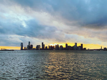 Sea by buildings against sky during sunset