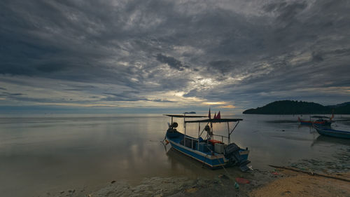 Boat moored on sea against sky during sunset