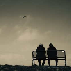 Rear view of man and woman sitting on bench against sky