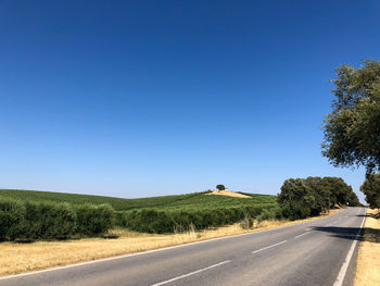 Country road amidst landscape against clear blue sky