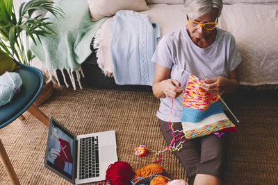 Senior woman learning knitting wool through laptop at home