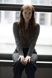 Portrait of young woman sitting against window