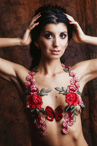 Portrait of shirtless young woman with floral decoration standing against wall