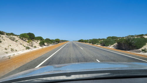 Road seen through car windshield against clear blue sky