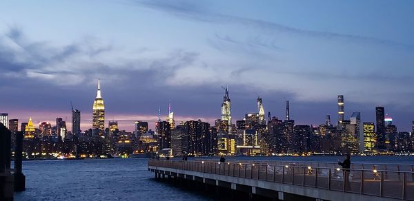 Illuminated skyline  of manhattan against cloudy sky