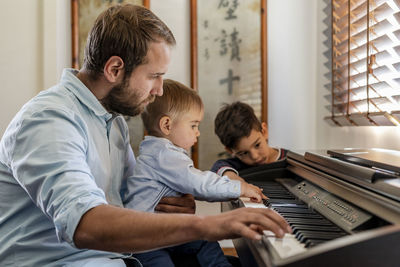 Father teaching piano to sons at home
