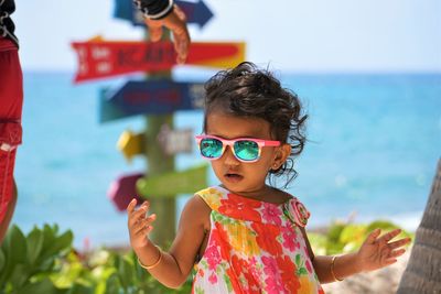 Cute baby girl wearing sunglasses standing at beach