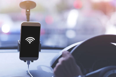 Cropped hand on steering wheel with wifi icon on smart phone in car