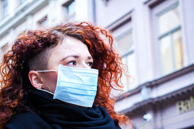 Close-up of woman wearing mask against building in city