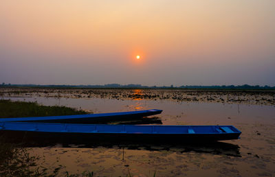 Boat moored on lake against sky during sunset