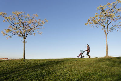 Man walking with baby stroller on field against sky