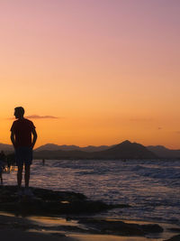 Rear view of silhouette man standing on beach during sunset