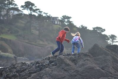 Rear view of siblings on rock against sky