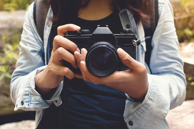 Midsection of woman adjusting camera lens outdoors