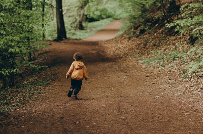 Rear view of boy walking on road in forest