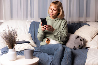 Young woman using mobile phone while sitting on sofa at home