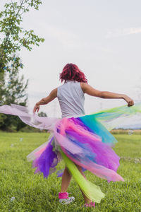 Rear view of woman dancing on field against trees