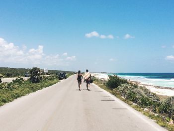 Rear view of people walking on road against blue sky at beach