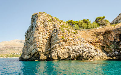 Rock formations by sea against clear blue sky