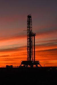 Silhouette drilling rig during sunset against sky