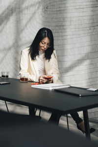 Mid adult businesswoman using mobile phone at table in office