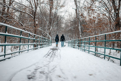 Rear view of man and woman walking on snow covered footbridge