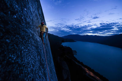 Side view man rock climbing at night above the sea and highway