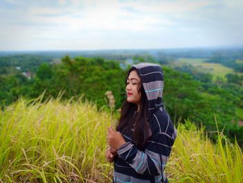 Young woman standing on field against sky