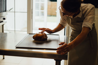 Female baker in uniform is decorating bread while working in bakery