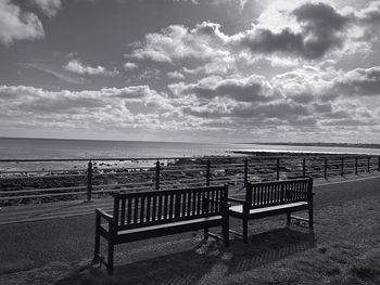 Empty bench on beach against sky