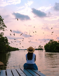 Rear view of man sitting on pier against lake during sunset