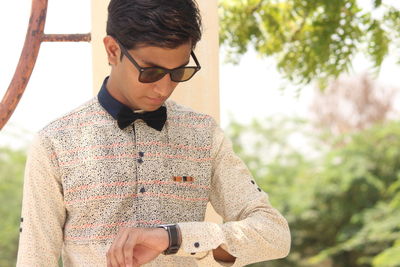Young man wearing sunglasses standing against trees