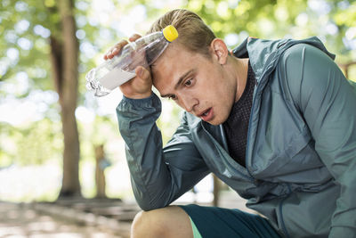 Tired man panting while holding water bottle after workout at park