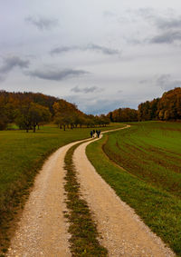 Dirt road amidst field against sky