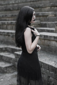 Side view of young woman standing against built structure