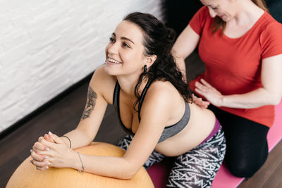 Fitness instructor assisting pregnant woman while exercising at home
