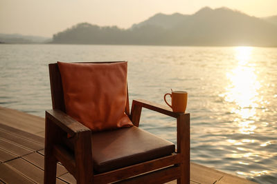 Empty chair by sea against sky during sunset