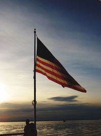 Silhouette flag by sea against sky during sunset