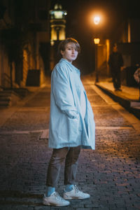 Portrait of woman standing on footpath at night