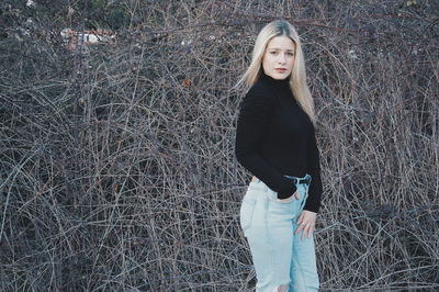 Portrait of young woman with hand in pocket standing against barbed wire