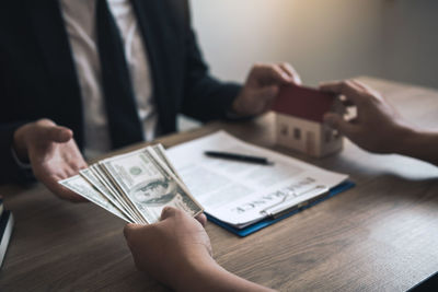 Cropped hand of customer giving paper currency to real estate agent on table