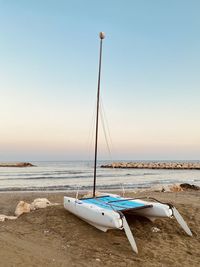 Catamaran on sandy beach in the mediterranean bay, sea in distance, under the clear sky.