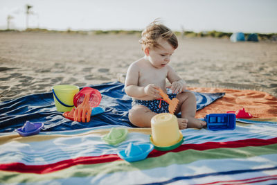 Baby boy playing with toys at beach during sunset