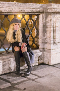 Portrait of smiling young woman sitting on brick wall