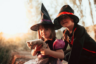 Portrait of girl with brother wearing costume holding teddy bear during halloween at forest