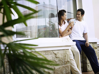 Smiling couple talking while having coffee against wall