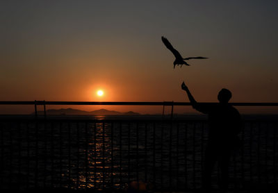 Silhouette man standing by sea against sky during sunset