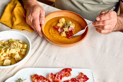 Man eating pumpkin cream soup with roasted bacon and croutons in clay plate on the table